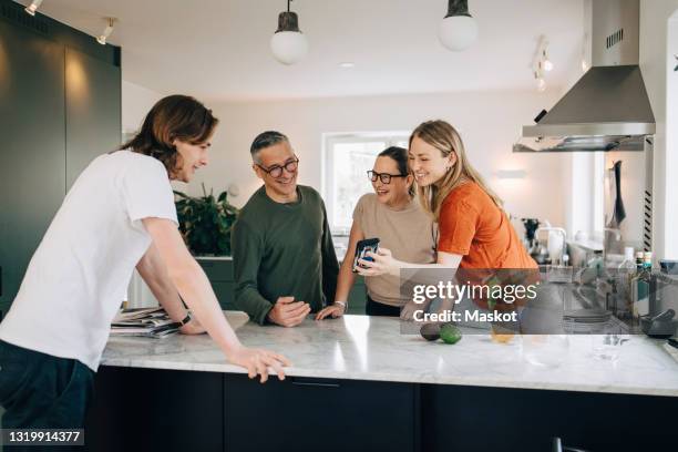 young woman showing smart phone to brother and parents in kitchen at home - vuxet barn bildbanksfoton och bilder