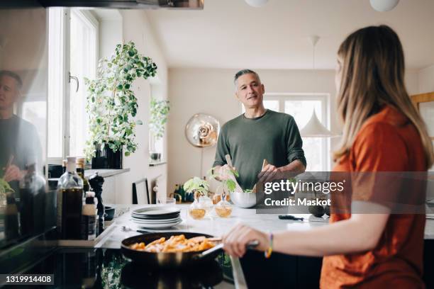 mature man preparing food while talking with daughter in kitchen at home - daughter cooking stock pictures, royalty-free photos & images