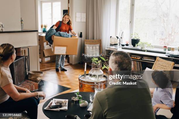 happy young woman carrying box looking at family while arriving at home - adult children with parents stockfoto's en -beelden