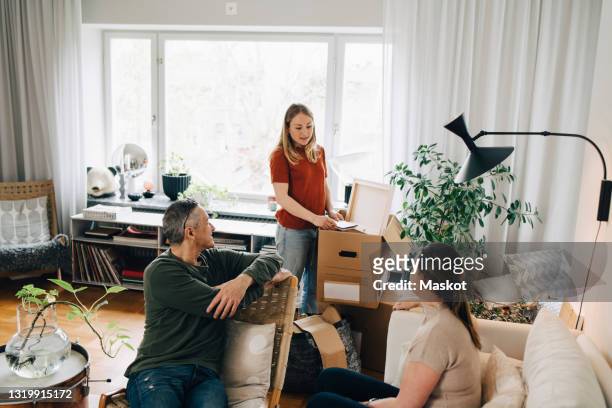young woman talking with parents while unpacking box in living room at home - erwachsene kinder stock-fotos und bilder