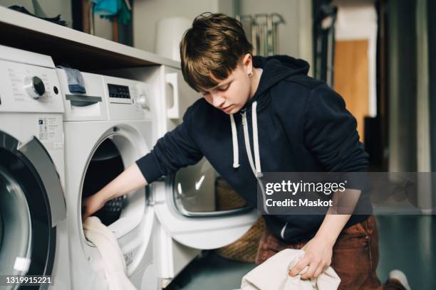 transgender person putting clothes in washing machine while doing chores at home - dryer stock-fotos und bilder