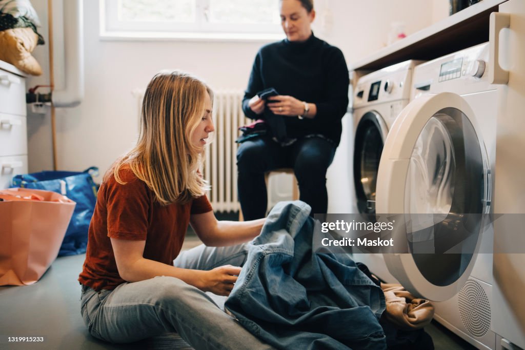 Young woman putting clothes in washing machine at utility room