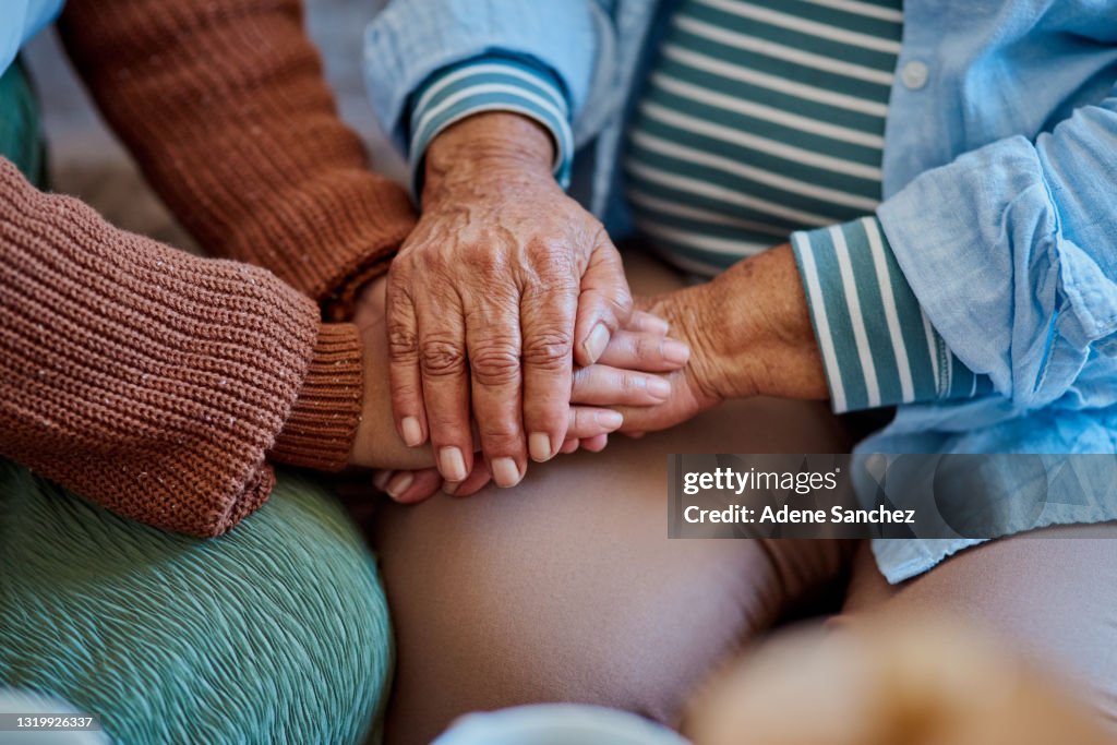Shot of an unrecognisable woman holding hands with her elderly relative on the sofa at home