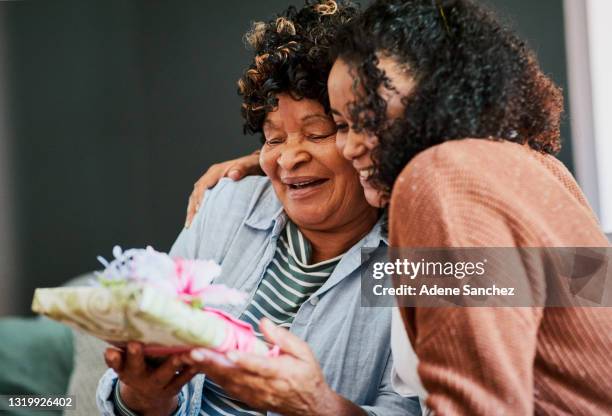 shot of a young woman giving her elderly relative a present on the sofa at home - senior birthday stock pictures, royalty-free photos & images