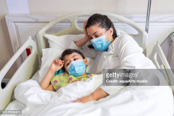 young mother lying on the hospital bed with sick kid wearing protective face mask - childhood cancer stock pictures, royalty-free photos & images