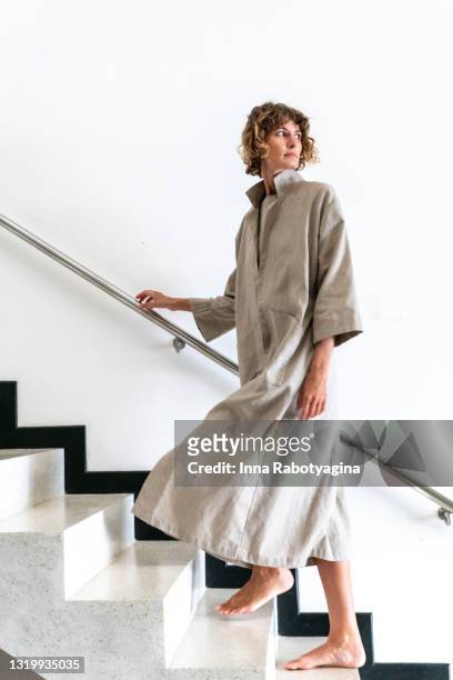 young adult woman inn long beige coat walking on minimalistic stairs against white wall - trench stock photos et images de collection
