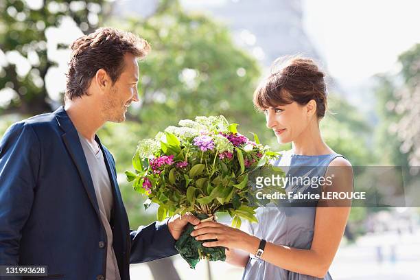 man giving a bouquet of flowers to a woman with the eiffel tower in the background, paris, ile-de-france, france - man giving flowers foto e immagini stock