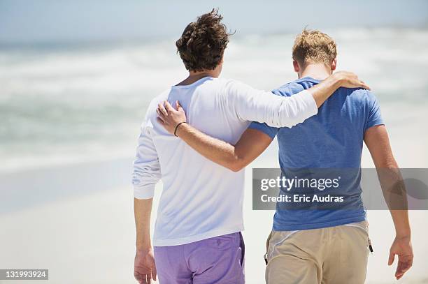 rear view of two men walking with their arms around each other - arm around back stock pictures, royalty-free photos & images