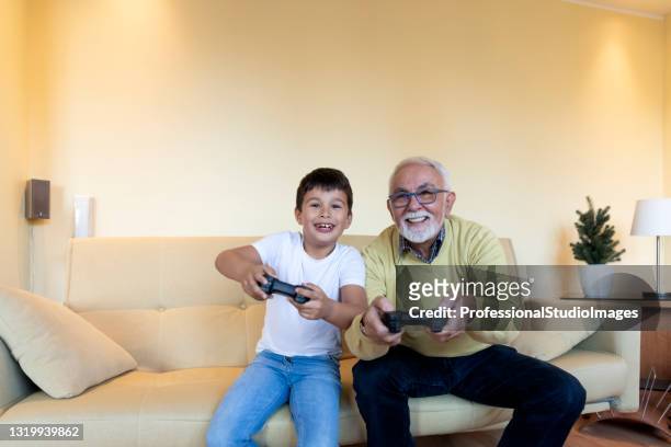 smiling boy y su abuelo están jugando videojuegos juntos en casa. - reality tv fotografías e imágenes de stock