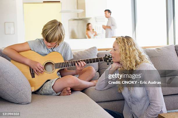 teenage boy playing a guitar and his mother listening - mom flirting fotografías e imágenes de stock