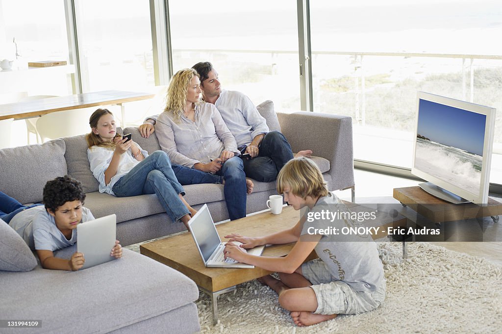 Couple watching television set while kids busy using electronic gadgets
