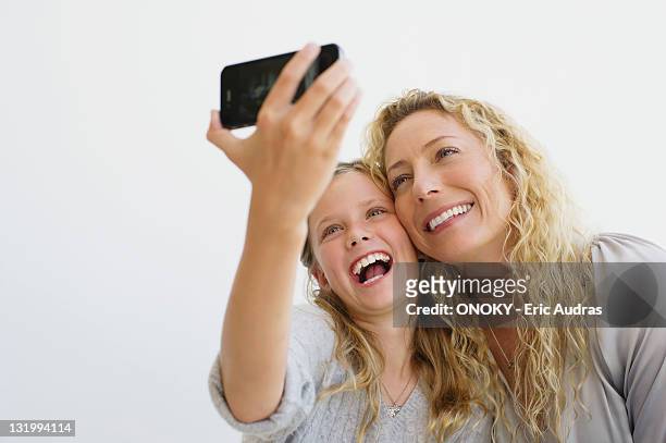 girl with her mother taking picture of themselves with a mobile phone - taking selfie white background stock-fotos und bilder