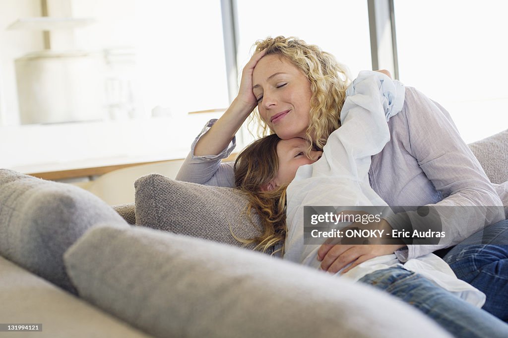 Mid adult woman and her daughter hugging each other on a couch