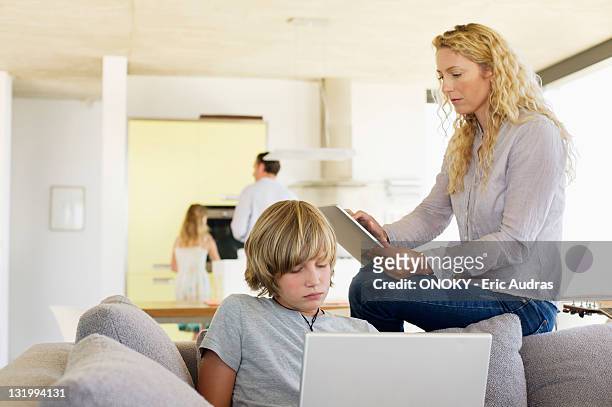 teenage boy using a laptop and his mother using a digital tablet - mother and son using tablet and laptop stock pictures, royalty-free photos & images