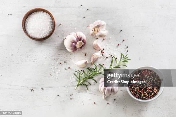 top view of a white desk with bowls full of sals and various peppers and garlic bulbs with rosemary. - seasoning - fotografias e filmes do acervo