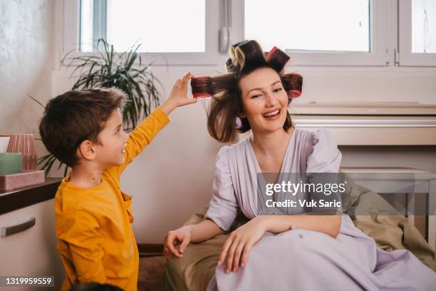 son taking out his mother hair curlers - hair curlers stockfoto's en -beelden