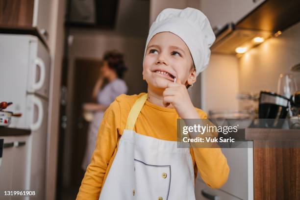 chico con la gorra de chef y uniforme lamiendo una piruleta - mini chef fotografías e imágenes de stock