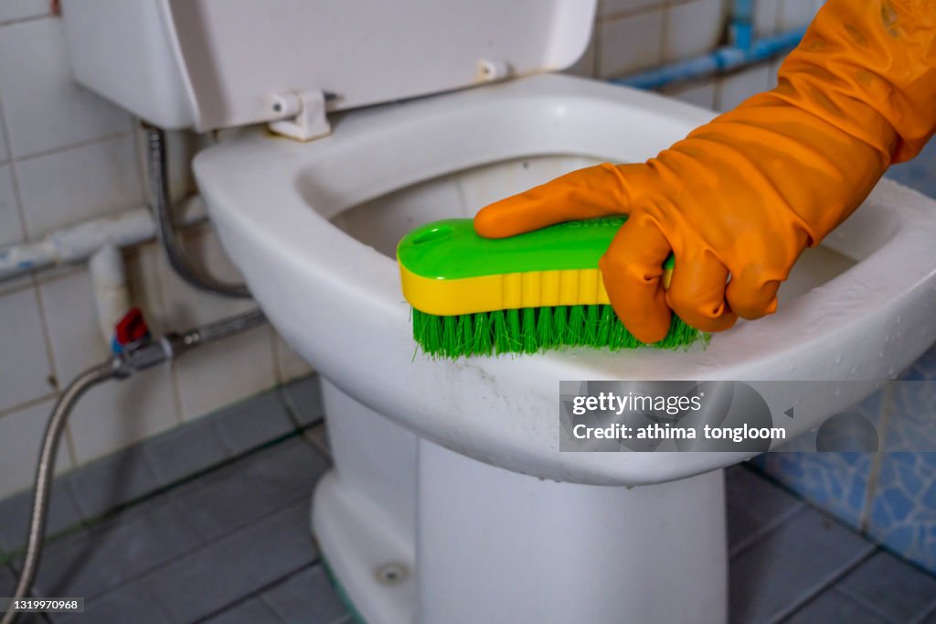 Close up of female hands wearing protective gloves, scrubbing toilet with brush