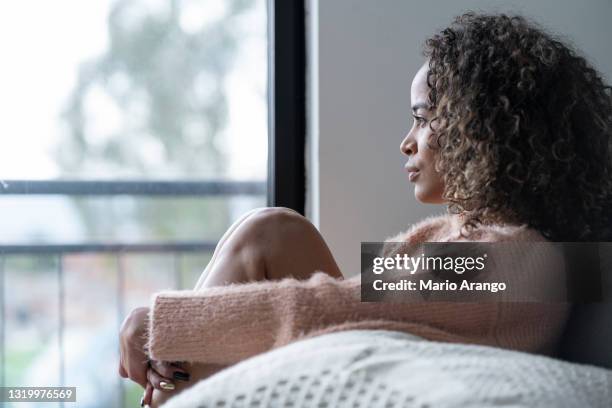 black woman sitting in the living room of her house looking away very shaken by her problems - anxiety disorder stock pictures, royalty-free photos & images