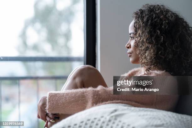 black woman sitting in the living room of her house looking away very shaken by her problems - invisible disability stock pictures, royalty-free photos & images
