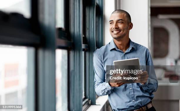 ontsproten van een jonge zakenman die een digitale tablet met behulp van terwijl zich bij een venster in een bureau bevindt - cheer stockfoto's en -beelden