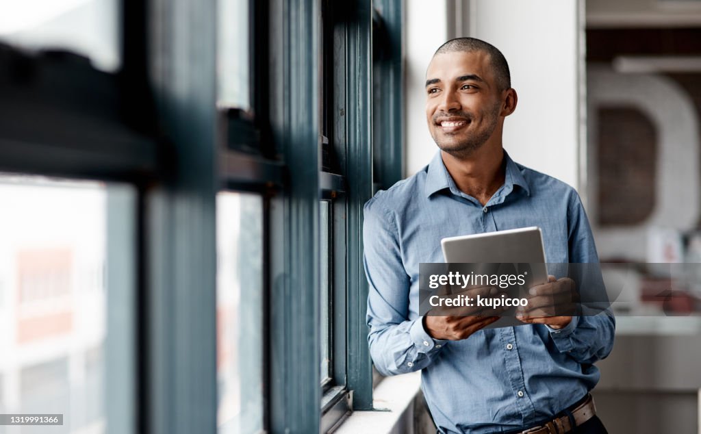 Shot of a young businessman using a digital tablet while standing at a window in an office
