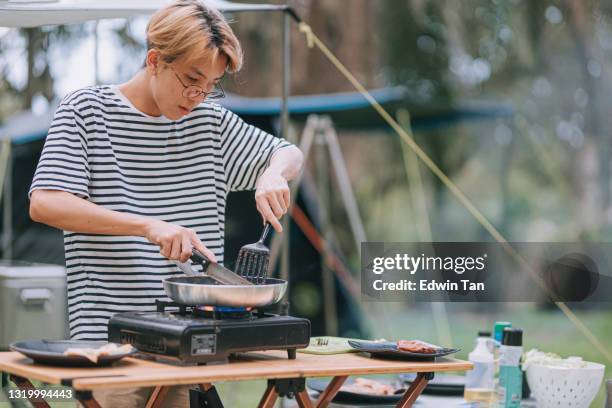 asian chinese teenage boy cutting pan fried chicken cooking for his family at camping tent - camping stove stock pictures, royalty-free photos & images