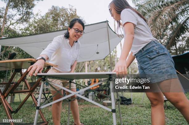 low-winkel-ansicht asiatische chinesische mutter und tochter einrichtung picknicktisch für die zubereitung von lebensmitteln auf dem campingplatz - zusammenklappbar stock-fotos und bilder