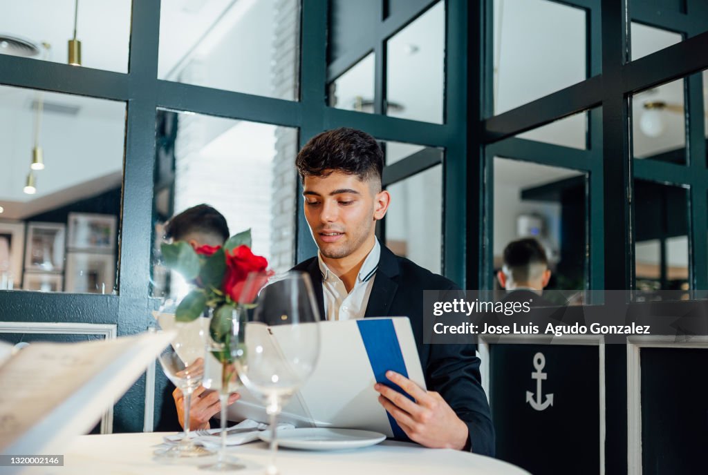 Young man is reading the menu in a fancy restaurant.