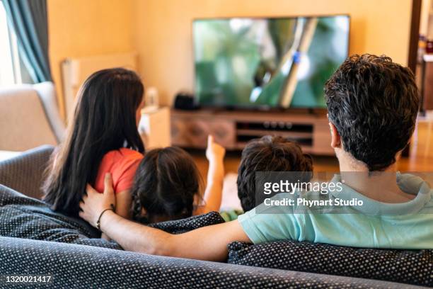 eltern und ihre beiden kinder schauen zu hause gemeinsam fern - begeistert fernsehen stock-fotos und bilder