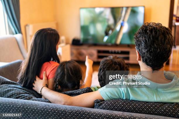 i genitori e i loro due figli guardano la tv insieme a casa - guardare la tv foto e immagini stock