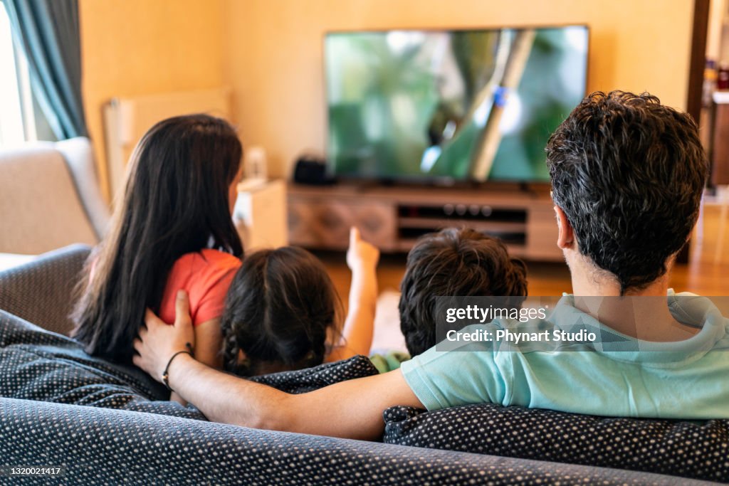 Parents and their two children watching TV together at home