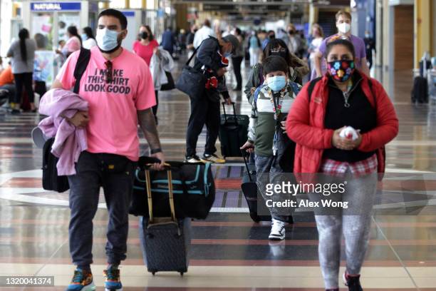 Travelers walk through the concourse with their luggage at Ronald Reagan Washington National Airport May 25, 2021 in Arlington, Virginia. According...