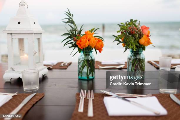 small orange roses in glass jar centerpiece with lanterns - candle sets stock-fotos und bilder