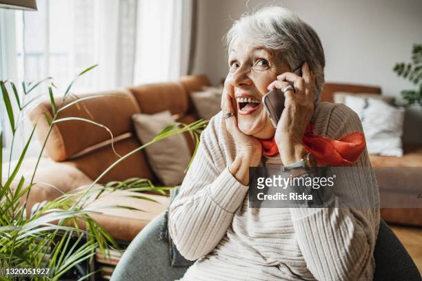 senior woman at home, smiling and talking on the phone - funny face woman stock pictures, royalty-free photos & images