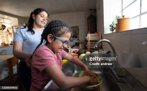 latin american girl helping her mother cook dinner in the kitchen - single mother poor stock pictures, royalty-free photos & images