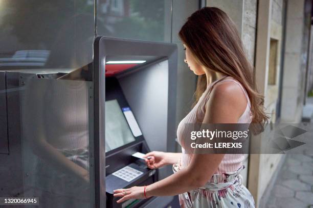 young brunette withdrawing money from an atm credit card - inserting stock-fotos und bilder