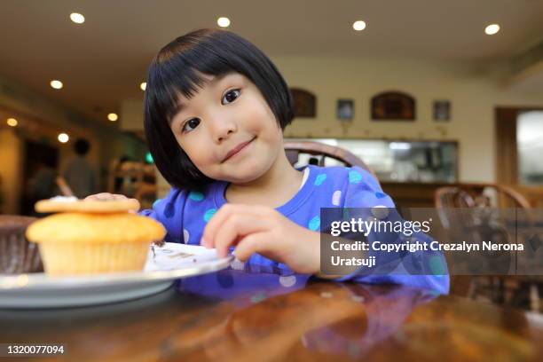 mixed race little girl with cupcake looking at camera - cupcakes girls stock-fotos und bilder