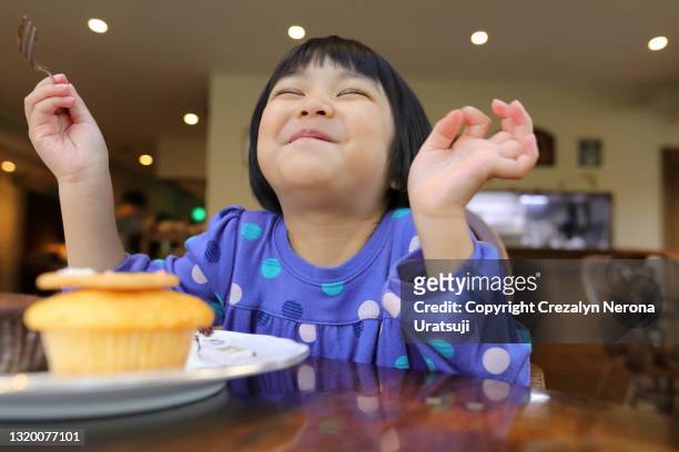 cute little girl smiling with eyes closed satisfied with cupcake dessert - cupcakes girls fotografías e imágenes de stock