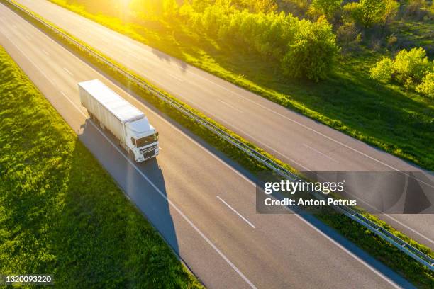 aerial view of truck driving on asphalt road along the green fields in rural landscape. - delivery truck stock-fotos und bilder