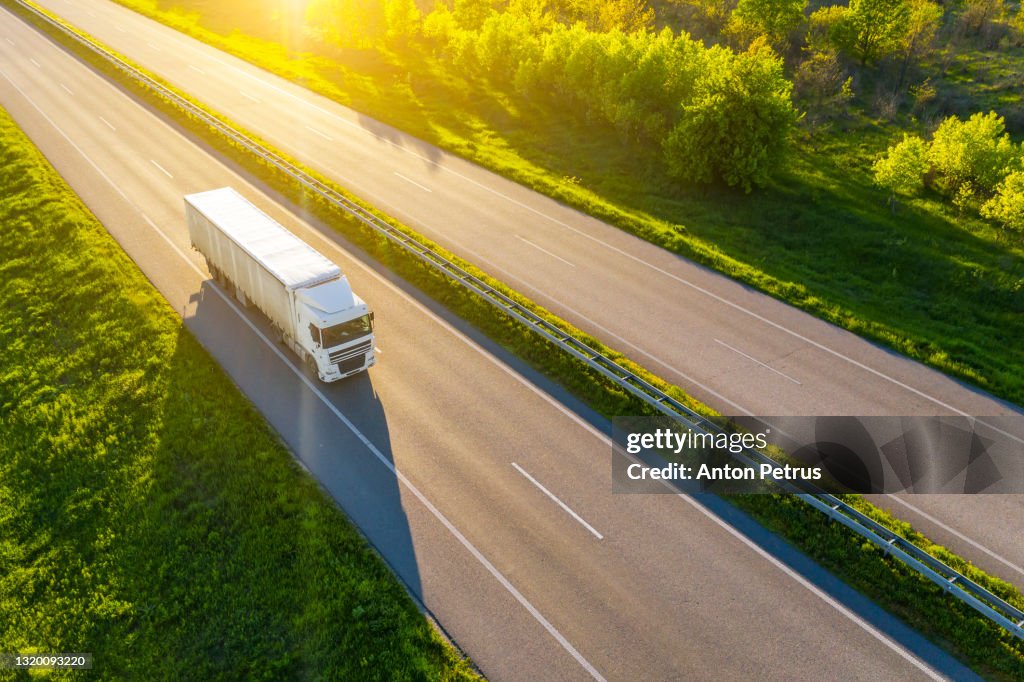 Aerial view of truck driving on asphalt road along the green fields in rural landscape.