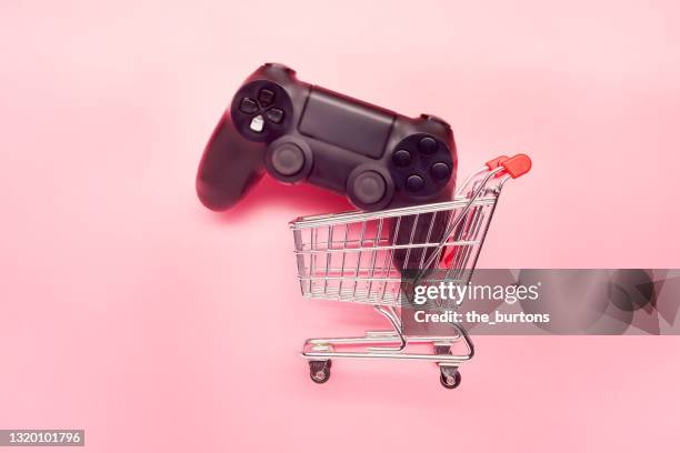 high angle view of game controller and small shopping cart on pink background - shopping electronics stock pictures, royalty-free photos & images