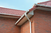 A close-up on plastic rain gutters, downspout, soffit and fascia with a box-end on the corner of a brick house as important parts of roofing system waterproofing and ventilation.