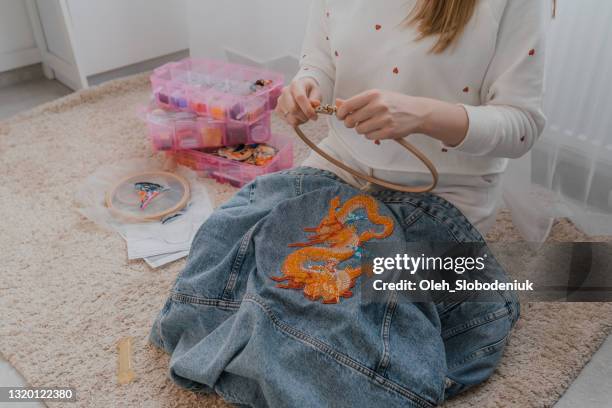 woman embroidering denim jacket with beads sitting on floor at home - denim jacket stock pictures, royalty-free photos & images