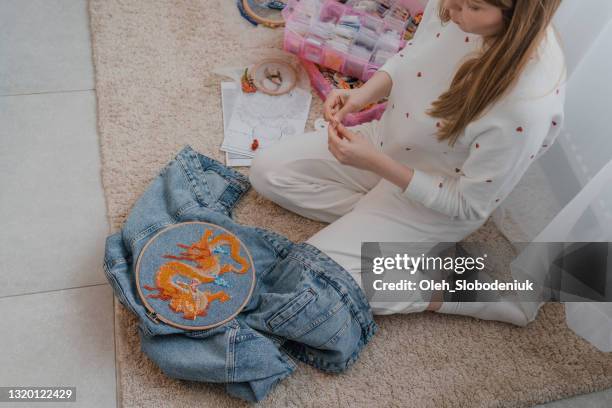 frau bestickt jeansjacke mit perlen, die zu hause auf dem boden sitzen - needlecraft stock-fotos und bilder