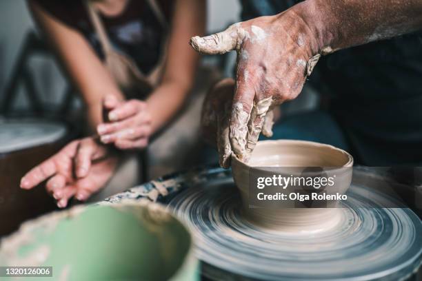 young woman instructor teaching a man to do pottery using a pottery wheel on a workshop - tonkeramik stock-fotos und bilder