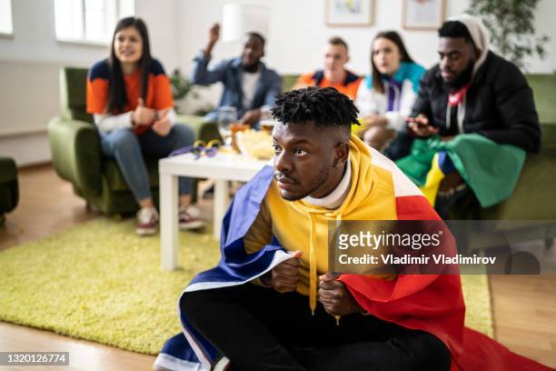 young man wrapped in a flag staring intently at a television - sports man cave stock pictures, royalty-free photos & images
