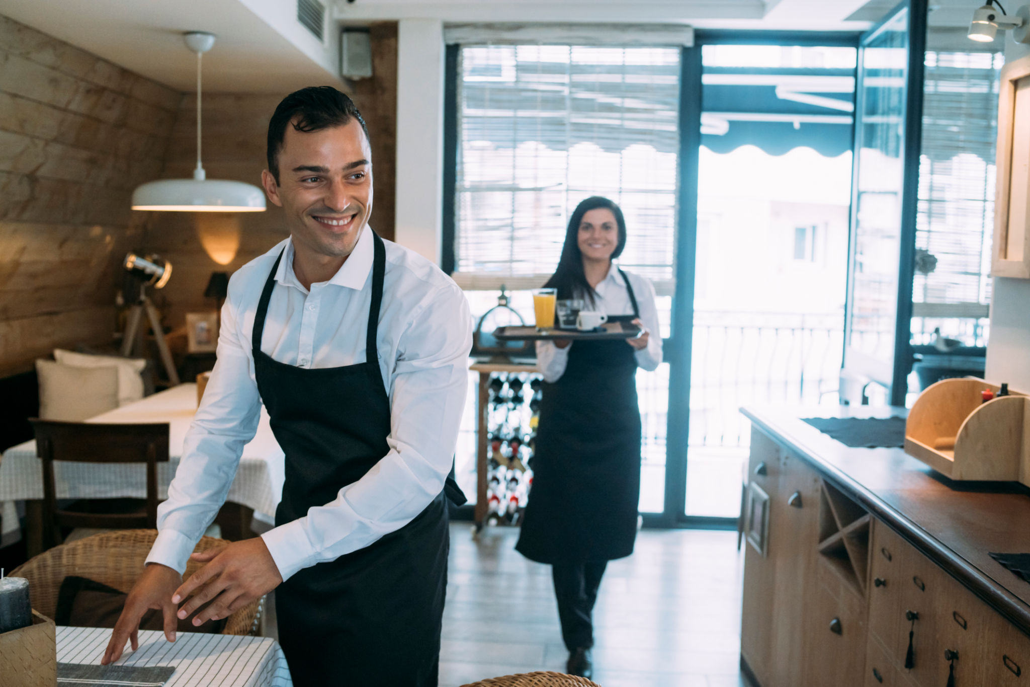 Cheerful young waiter and his female colleague during their work in the restaurant Cheerful young waiter and his female colleague during their work in the restaurant