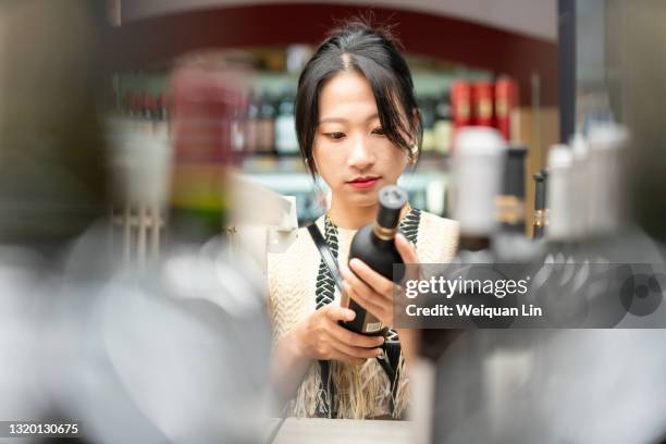 young asian woman is choosing red wine in the store - chinese young adults shopping imagens e fotografias de stock