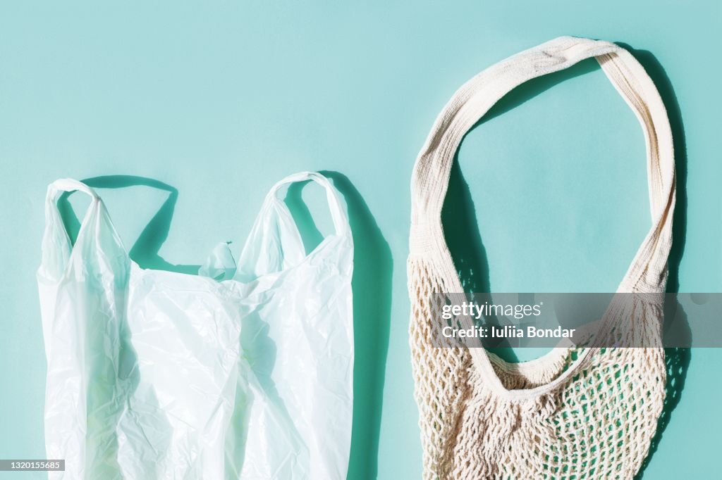 Plastic bag with eco natural mesh shopping bag, flat lay on blue background